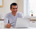 Mann sitzt vor Laptop und kauft online mit Karte ein