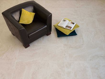 Carreaux en grès cérame fin, aspect travertin clair avec fauteuil noir et coussins colorés.