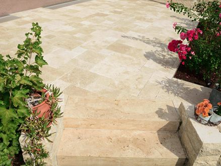 Photo du client : dalles de travertin Medium, tambourinées, assemblage romain, posées sur une terrasse, photo des marches d'escalier avec parterres de fleurs à gauche et à droite
