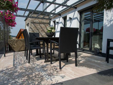 Une terrasse aménagée avec des meubles noirs et des dalles en travertin Natura effet bois