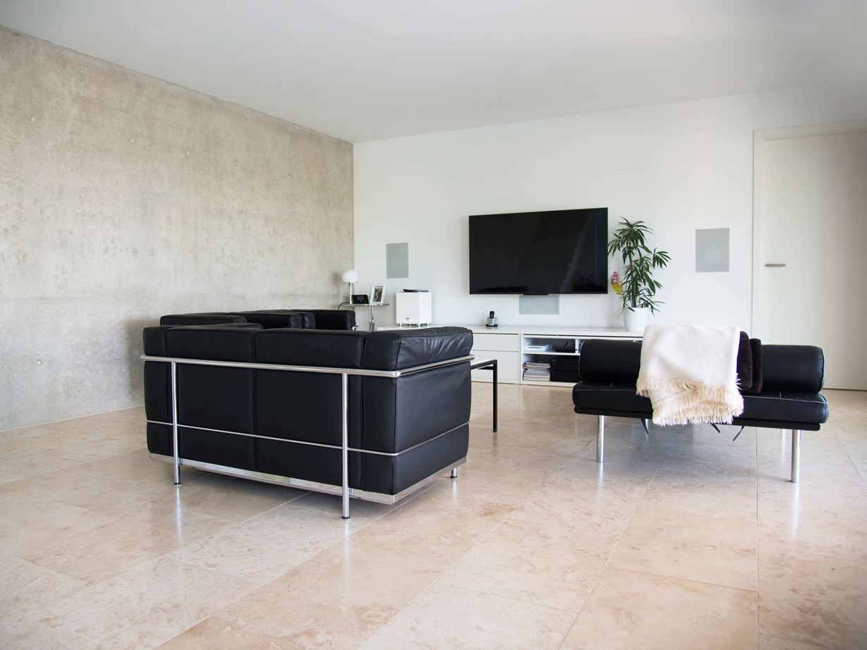 Salle de séjour moderne avec canapé noir et carreaux de travertin beige clair Classic Light comme revêtement de sol
