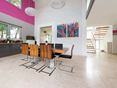Travertin beige et couleurs vives : une combinaison osée mais réussie Salle à manger ouverte avec chaises modernes en bois et tableaux colorés au mur, rêvetement de sol en travertin clair à la surface adoucie