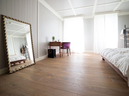 Chambre sol en bois et miroir adossé au mur sur la gauche dans le miroir on voit le reflet du lit