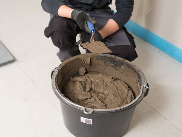 Fliesenleger vor einem Eimer mit Natursteinkleber